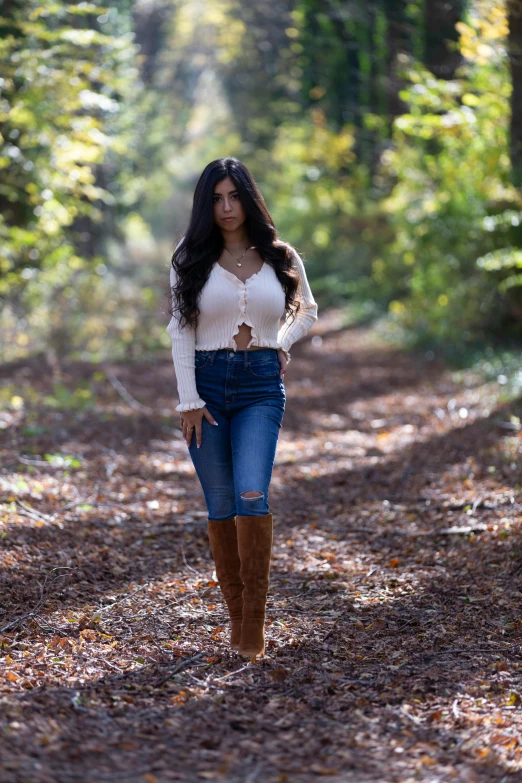 a woman walking down a path in the woods, by Robbie Trevino, wearing a camisole and boots, mia khalifa, fall season, ( ( ( wearing jeans ) ) )