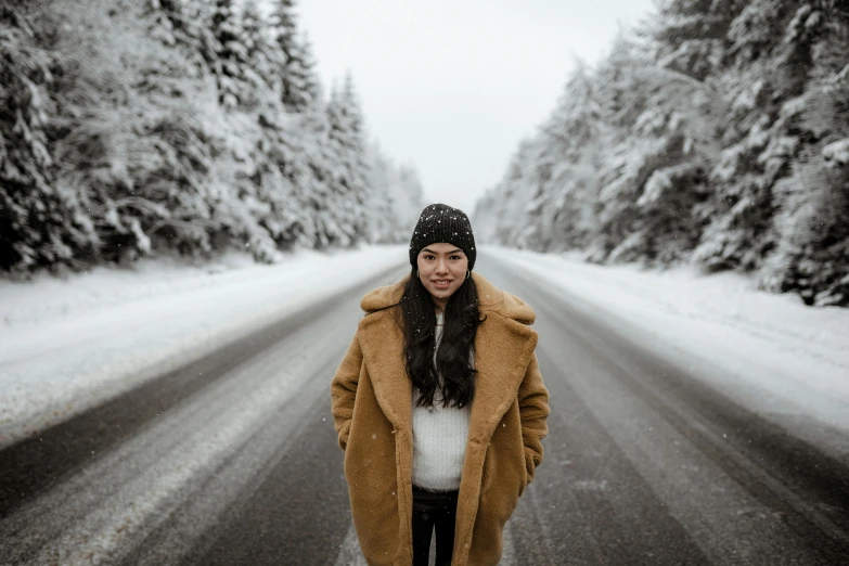 a woman standing in the middle of a snowy road, by Julia Pishtar, pexels contest winner, light brown coat, avatar image, portrait image, holiday season