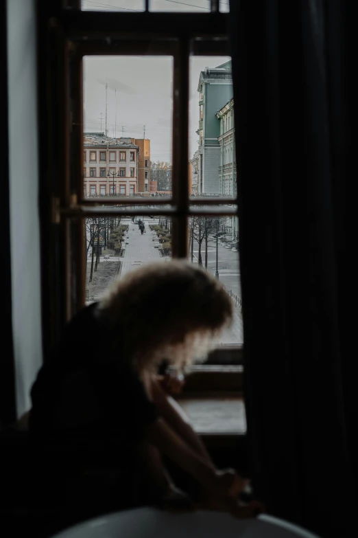 a woman sitting on a chair in front of a window, by Anna Boch, pexels contest winner, snowy day, view from the streets, helsinki, looking through a window frame