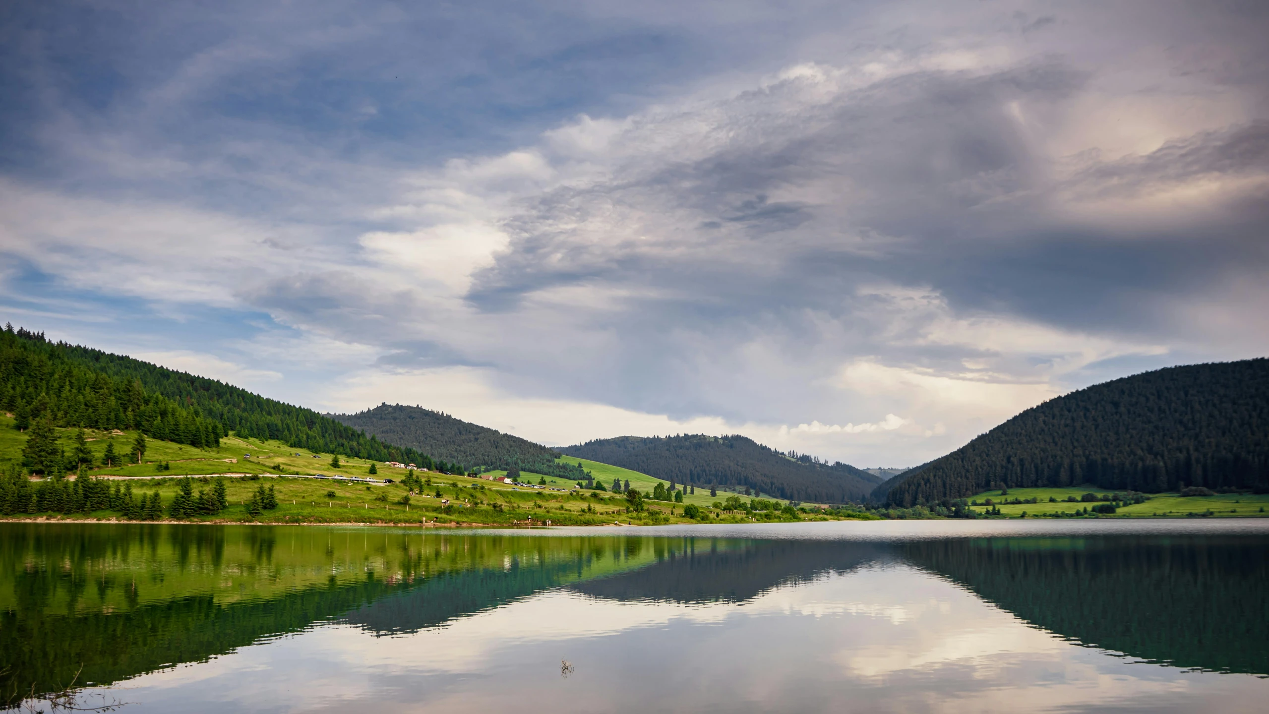 a large body of water sitting on top of a lush green hillside, by Muggur, pexels contest winner, lake reflection, transylvania, grey, big sky