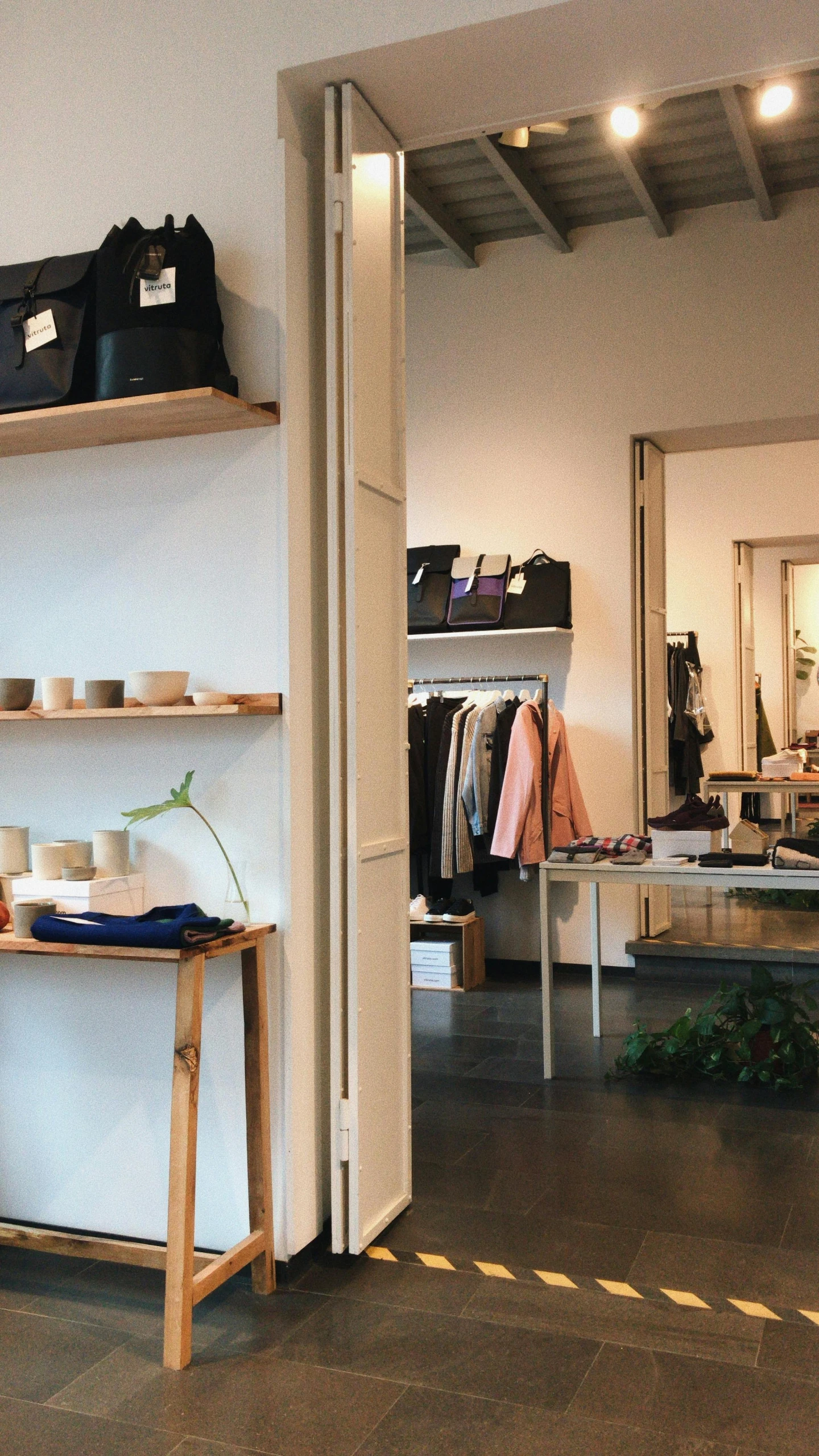 a woman sitting at a table in a clothing store, pexels, purism, panoramic shot, simple wood shelves, walking to the right, sustainable materials