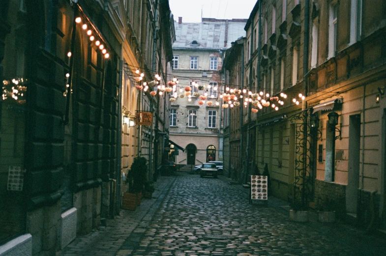 a cobblestone street with lights strung over it, inspired by Elsa Bleda, pexels contest winner, renaissance, lviv, gif, vintage photo