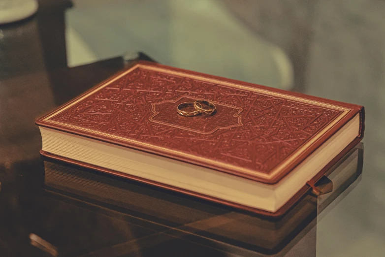 a book sitting on top of a table next to a clock, the ring, red and gold, thumbnail, notebook