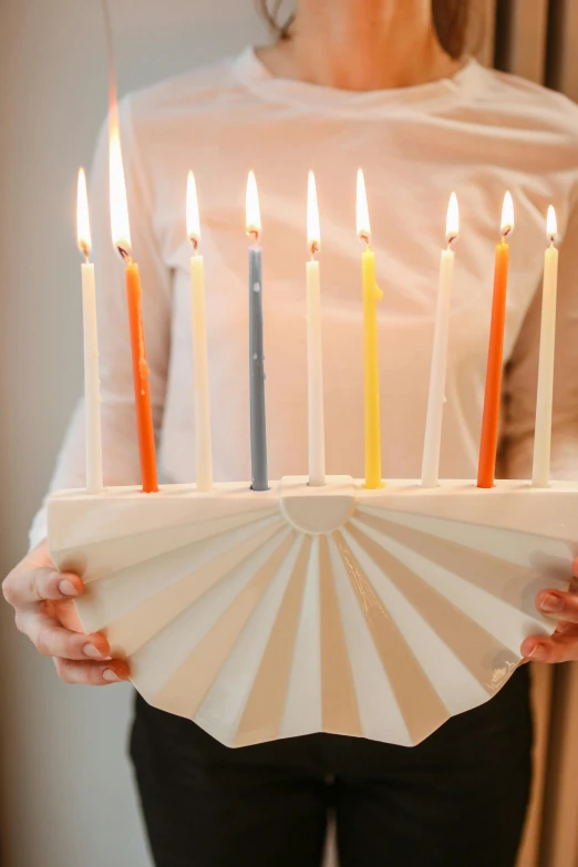 a woman holding a cake with candles on it, still of rainbow ophanim, white ceramic shapes, carrying a tray, front facing shot