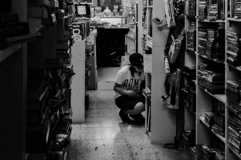 a black and white photo of a man in a store, pexels contest winner, digging, low quality footage, kneeling and looking up, busy but lonely