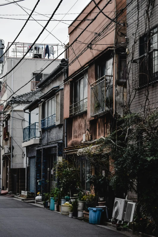 a city street filled with lots of tall buildings, a colorized photo, inspired by Miyagawa Chōshun, pexels contest winner, mingei, dilapidated houses, location of a dark old house, wires hanging across windows, けもの