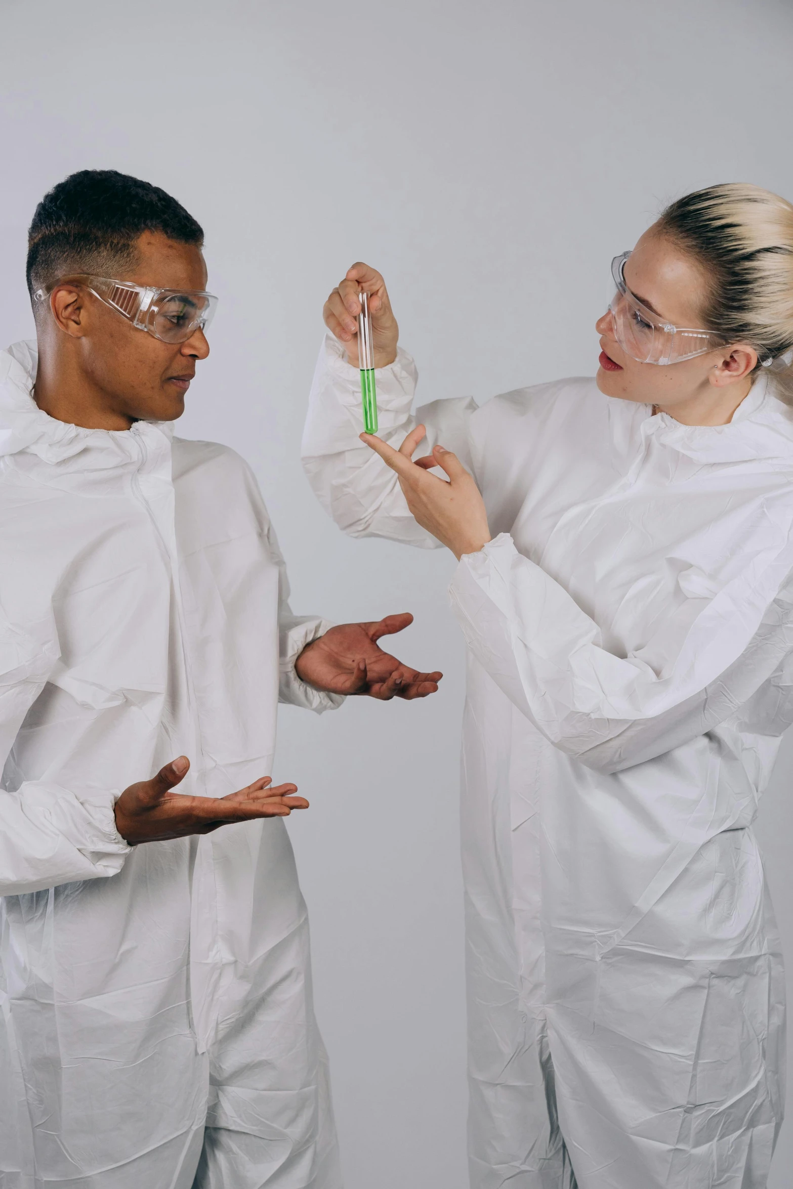 a couple of people standing next to each other, experimenting, flight suit and gloves, wearing lab coat and glasses, mix of ethnicities and genders