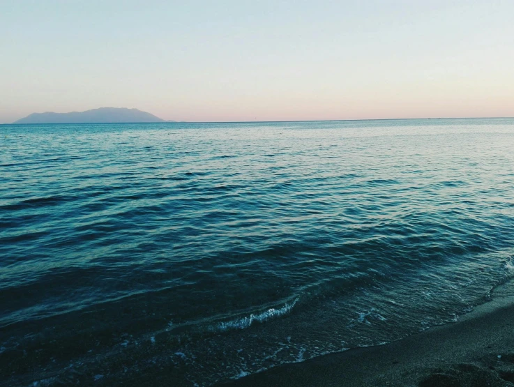 a man standing on top of a beach next to the ocean, unsplash, minimalism, late summer evening, blue and green water, gulf of naples, instagram post