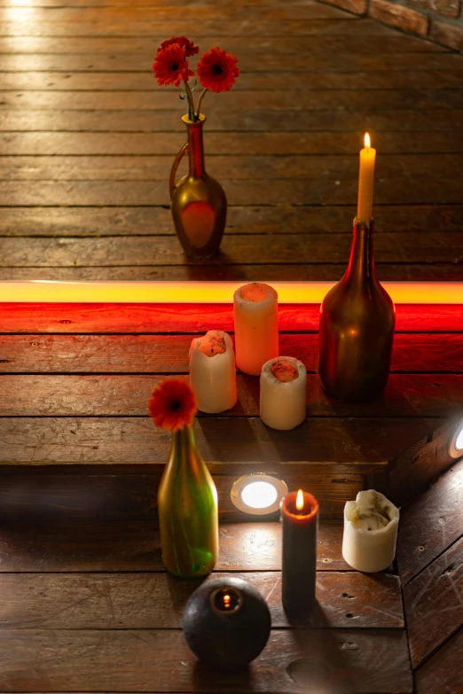 a group of candles sitting on top of a wooden floor, inspired by Henri Le Sidaner, light and space, bottles covered in wax, orange and red lighting, vases and bottles, day setting