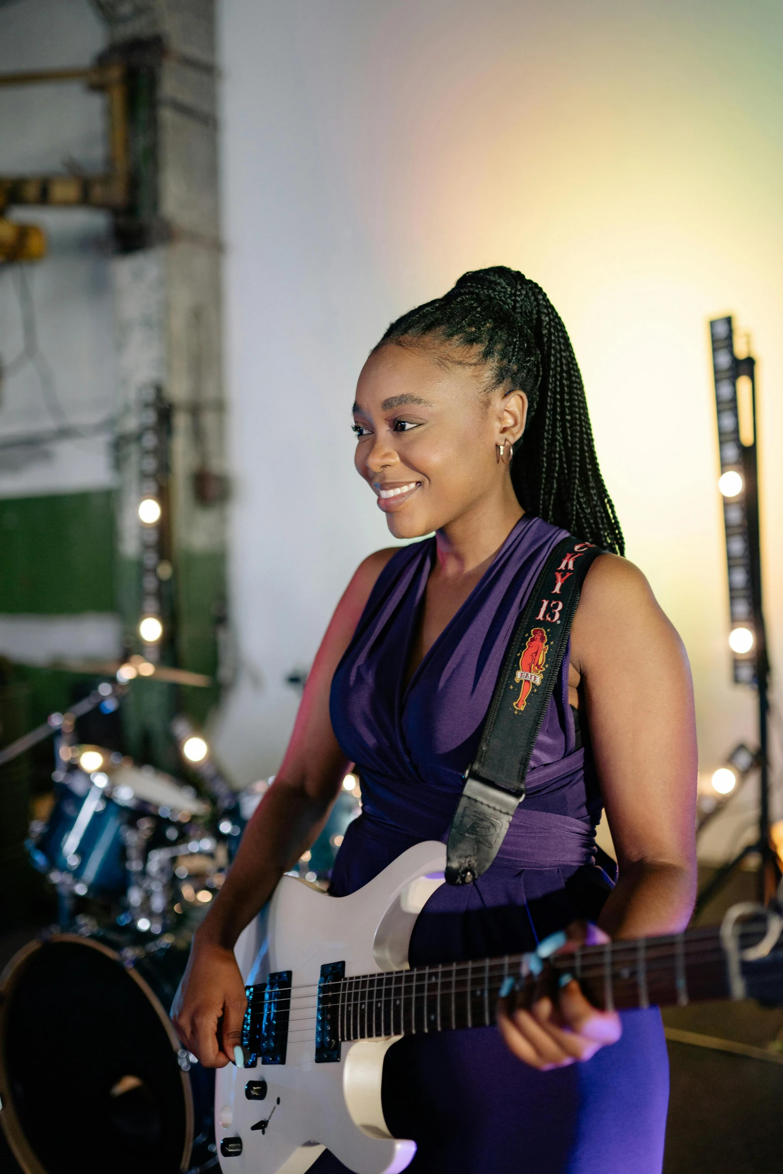 a woman in a purple dress playing a guitar, ashteroth, in a workshop, promotional image, slightly smiling