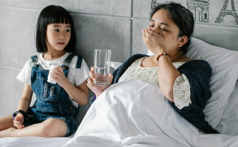 a woman laying in bed next to a little girl, pexels contest winner, hurufiyya, drinking cough syrup, plague and fever. full body, an asian woman, filled with water