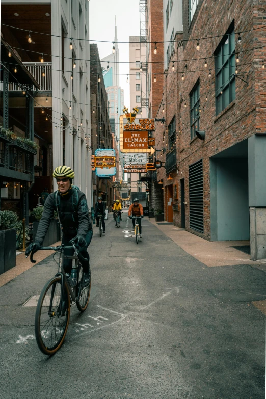 a man riding a bike down a street next to tall buildings, by Greg Rutkowski, pexels contest winner, location [ chicago ( alley ) ], neon signs in background, well built, kailee mandel