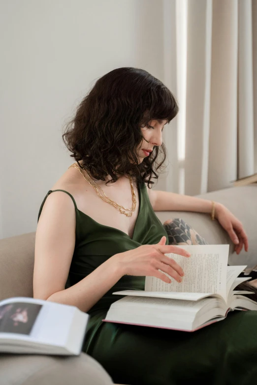 a woman sitting on a couch reading a book, inspired by Mathieu Le Nain, renaissance, she wears a dark green dress, song hye - kyo, japanese collection product, gold and pearl necklaces