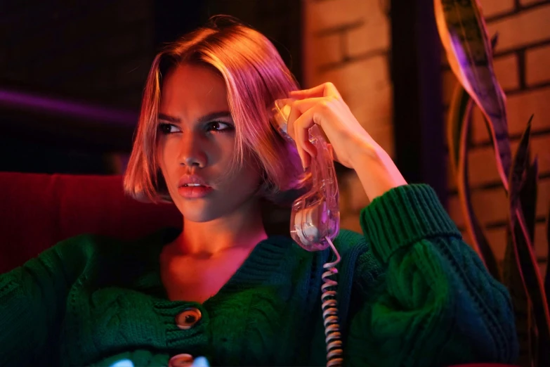 a woman sitting in a chair holding a phone to her ear, a colorized photo, inspired by Elsa Bleda, trending on pexels, magic realism, jessica alba woman, subtle neon underlighting, angry scarlett johansson, wearing a green sweater