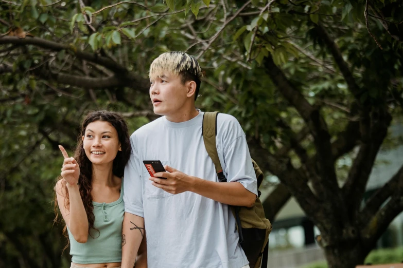 a man and a woman standing next to each other, trending on pexels, happening, looking at his phone, of taiwanese girl with tattoos, trees in the background, college students