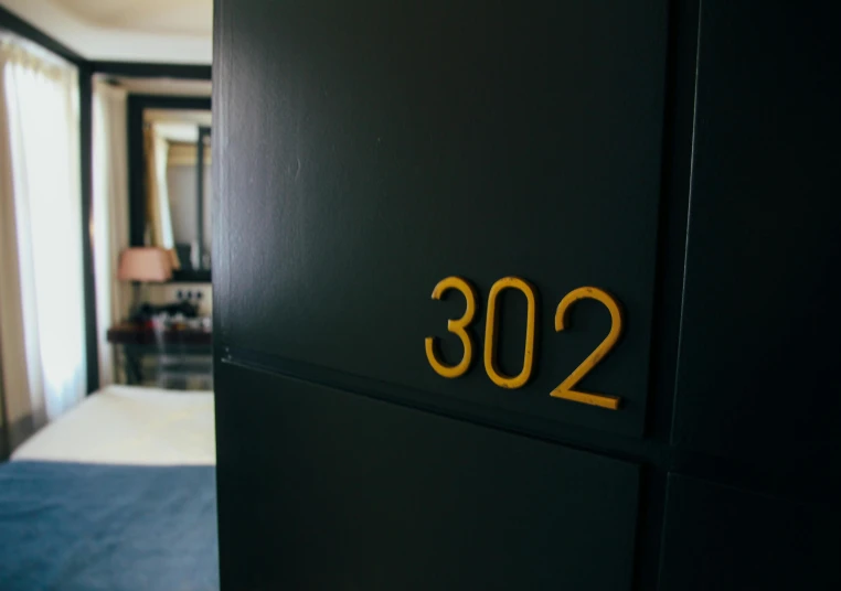 a close up of a door with a number on it, by Matt Cavotta, unsplash, apartment with black walls, yellow carpeted, 303, gold