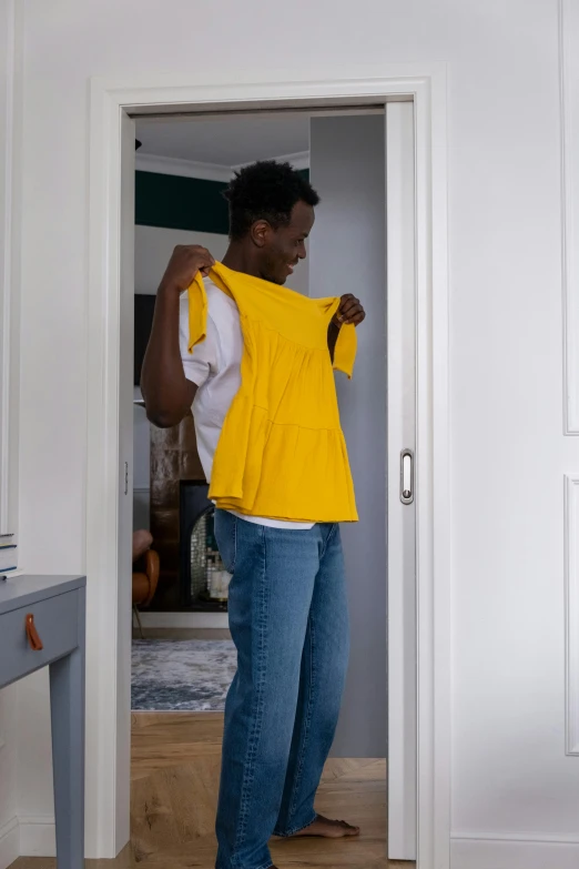 a woman in a yellow shirt standing in a doorway, by Francis Helps, male teenager, uncluttered, wearing tanktop, lined in cotton