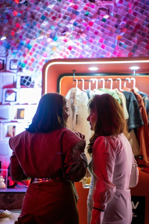 a couple of women standing in front of a mirror, neon standup bar, smart textiles, vendors, warmly lit