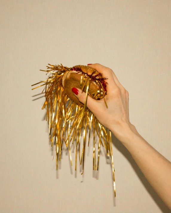 a person holding a gold item in their hand, an album cover, inspired by Méret Oppenheim, unsplash, rasquache, spikes, golden rainbow tubing, ignant, in style of juergen teller