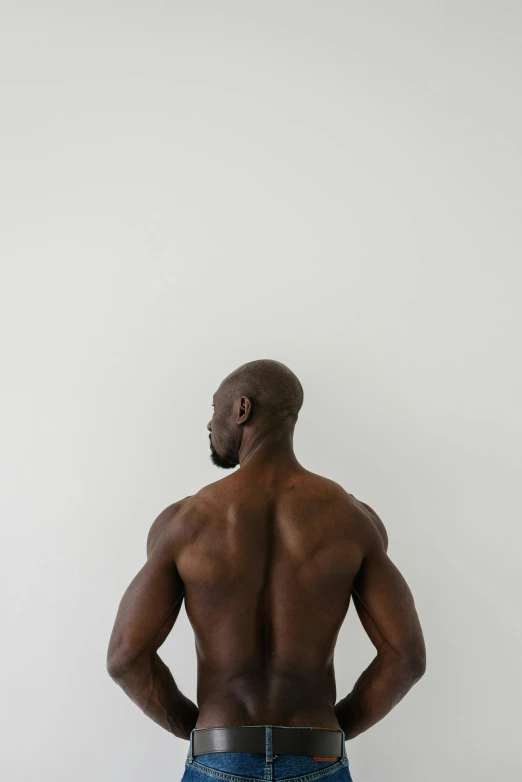 a man standing with his back to the camera, muscular characters, grey backdrop, black skin, big wide broad strong physique |