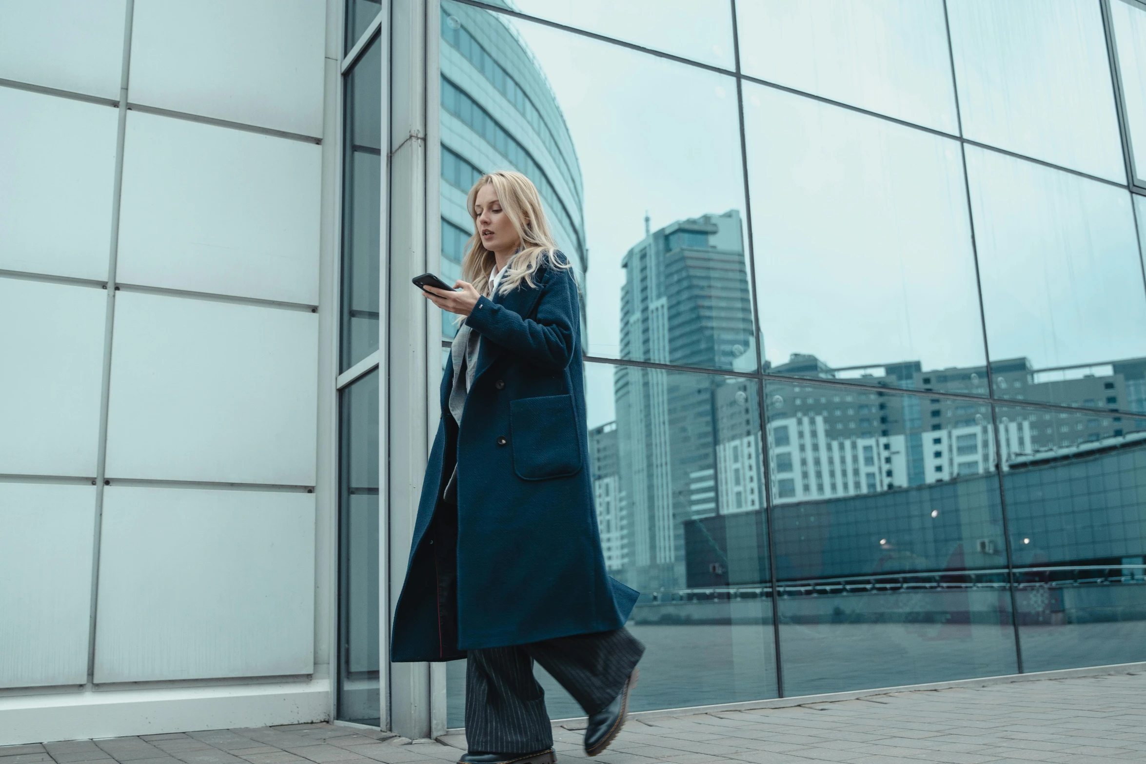 a woman standing in front of a building looking at her cell phone, by Emma Andijewska, pexels contest winner, walking to work, rosamund pike as the doctor, technological longcoat, glass ceilings