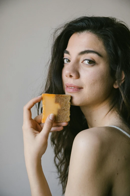 a woman holding a piece of cheese in her hand, trending on pexels, weathered olive skin, square face, soap, flan