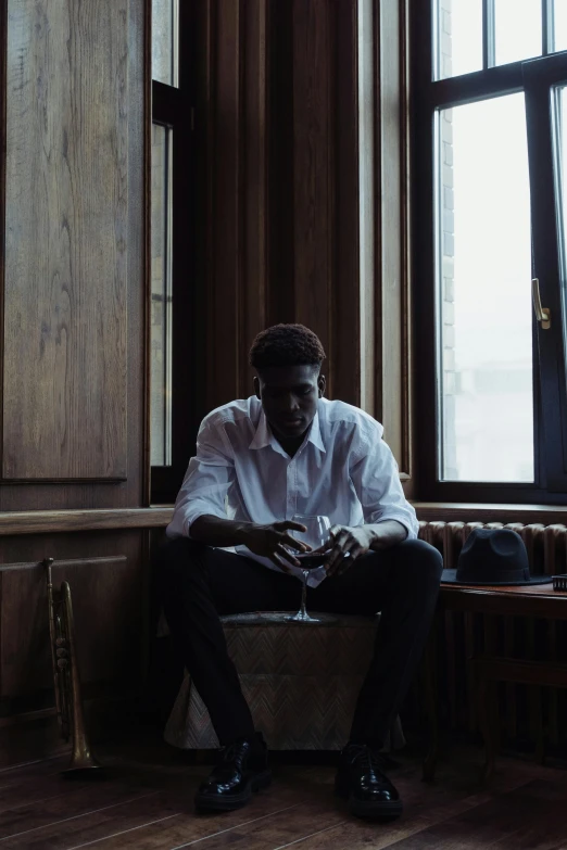 a man sitting on a bench in front of a window, an album cover, inspired by Gordon Parks, trending on unsplash, brown skinned, sitting at the bar, androgynous person, sitting in a waiting room