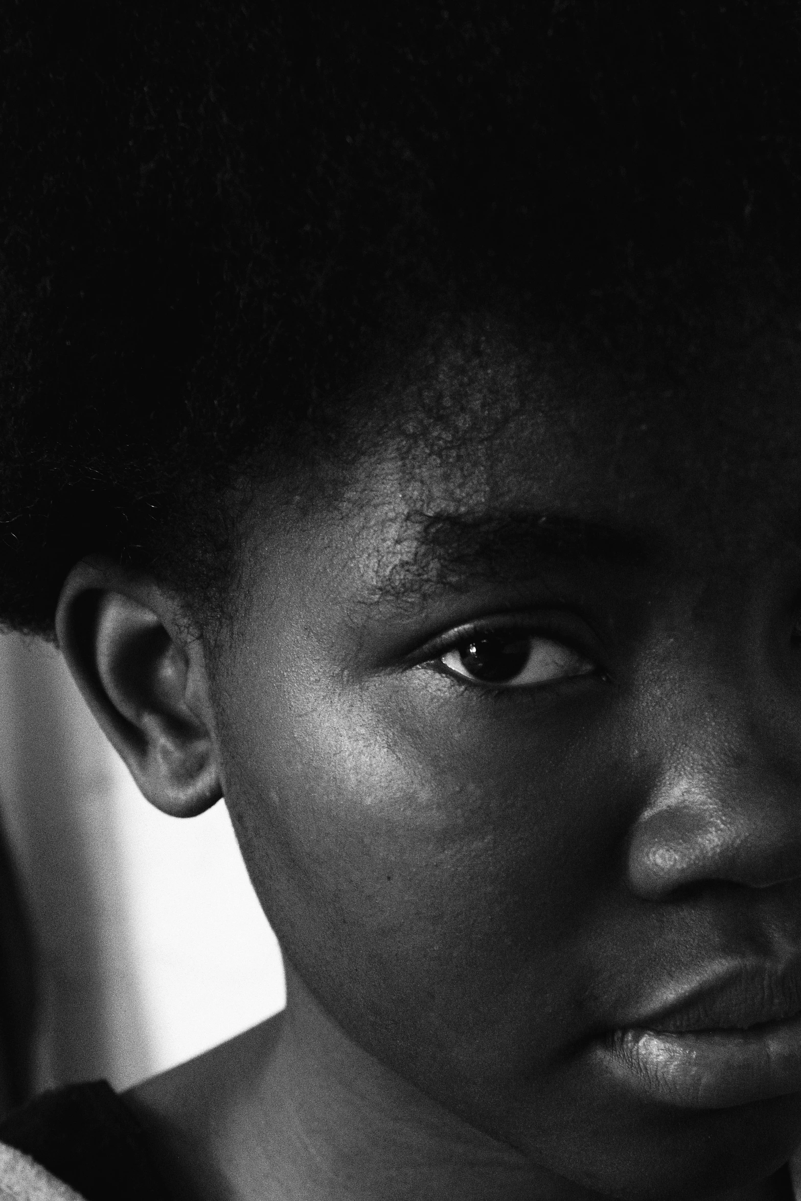a black and white photo of a young girl, inspired by Roy DeCarava, hyperrealism, afro hair, black teenage boy, eye of a woman, portrait featured on unsplash