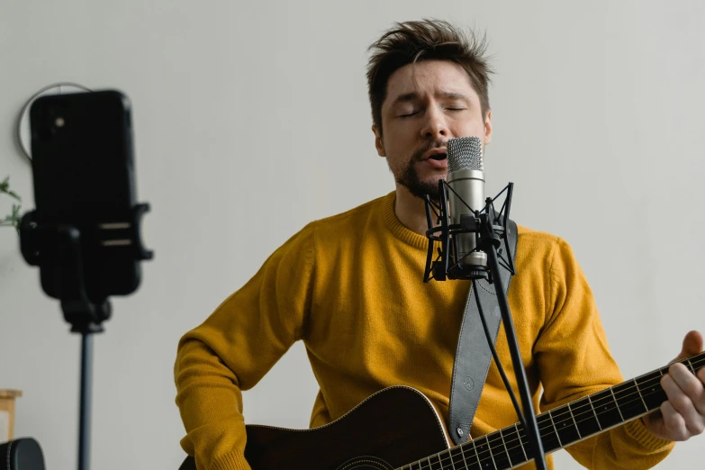 a man playing a guitar in front of a microphone, inspired by Justin Currie, pexels contest winner, he is wearing a brown sweater, avatar image, sitting in an empty white room, close up portrait photo