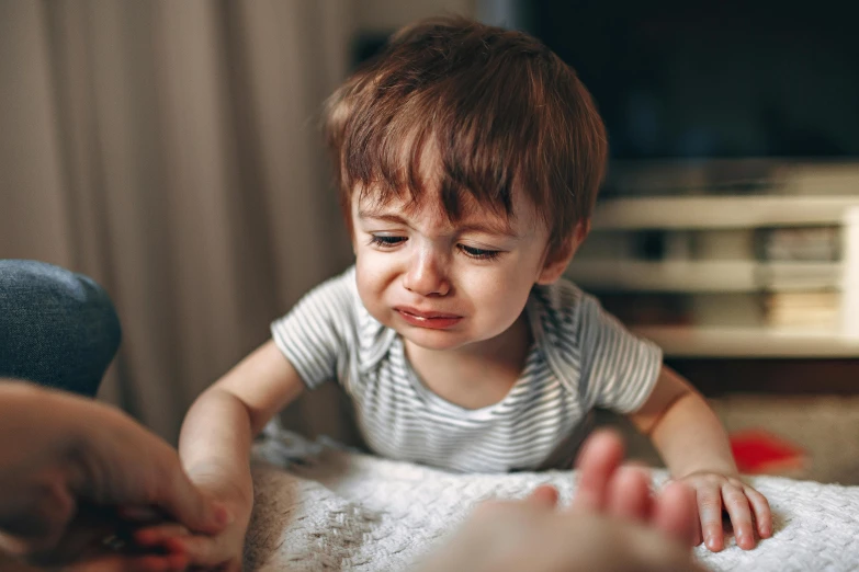 a little boy sitting on top of a bed next to a person, by Julia Pishtar, pexels, crying and puking, exhausted face close up, walking down, portrait of small