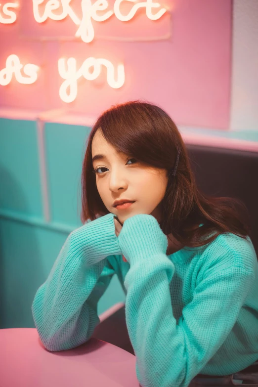 a woman sitting at a table in front of a neon sign, a colorized photo, inspired by Kim Jeong-hui, trending on pexels, realism, blue sweater, young adorable korean face, aesthetic cute with flutter, selfie shot straight on angle