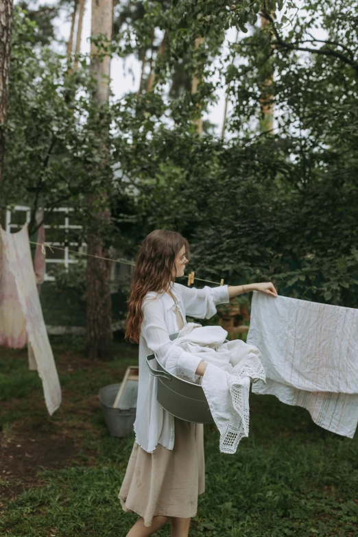 a woman hanging out her clothes on a clothes line, by Anna Boch, pexels contest winner, process art, wearing white pajamas, back yard, ukrainian girl, washing her dark long hair