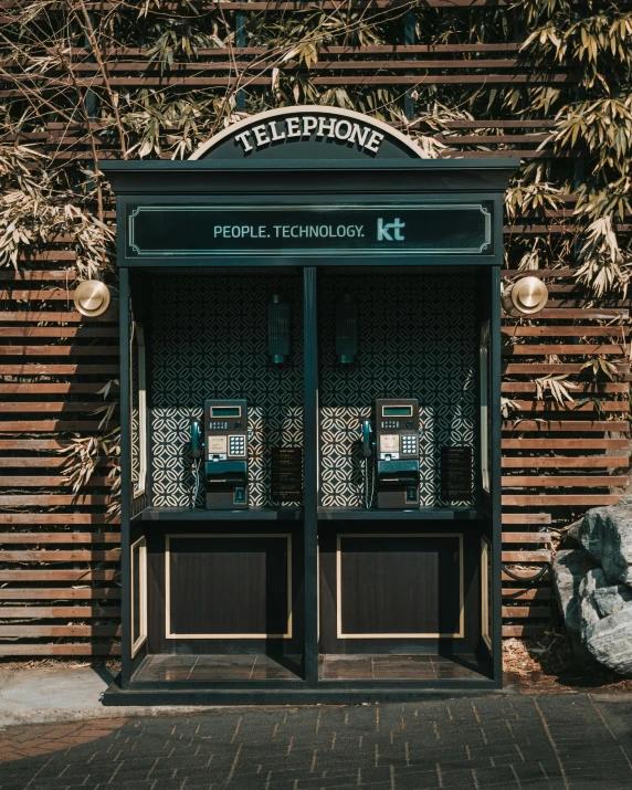 a telephone booth in front of a brick building, 2 people, cult of technology, kitsch, 2019 trending photo