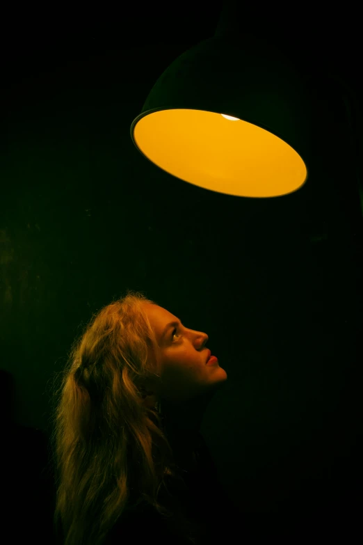 a woman looking up at a yellow light, by Adam Chmielowski, conceptual art, julia garner, atmospheric lighting - n 9, large head, a blond