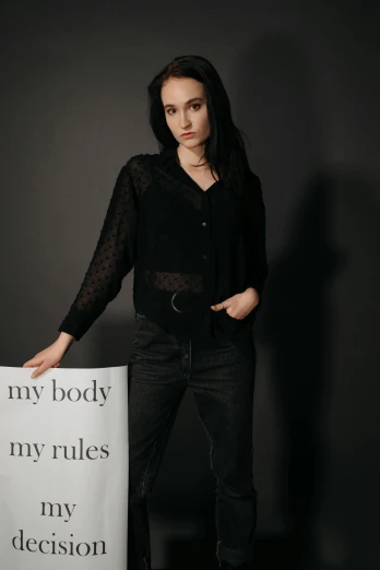 a woman standing next to a sign that says my body, my rules, my decision, pexels contest winner, antipodeans, very beautiful goth top model, transparent body, promotional image, black pants