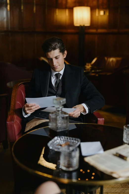 a man in a suit sitting at a table, by Alice Mason, unsplash, renaissance, speakeasy bar background, writing a letter, adam driver, ignant