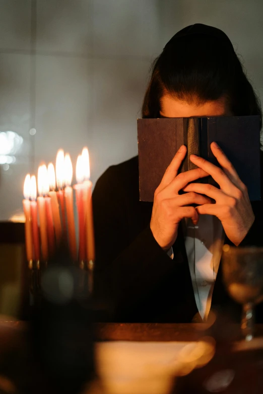 a woman holding a book in front of her face, an album cover, by Micha Klein, pexels, renaissance, glowing candles, orthodox, sad man, a seance