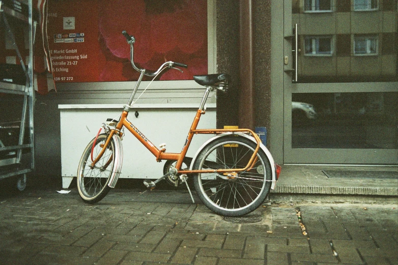 an orange bicycle parked in front of a building, colored analog photography, folded, on hasselblaad, analog photograph