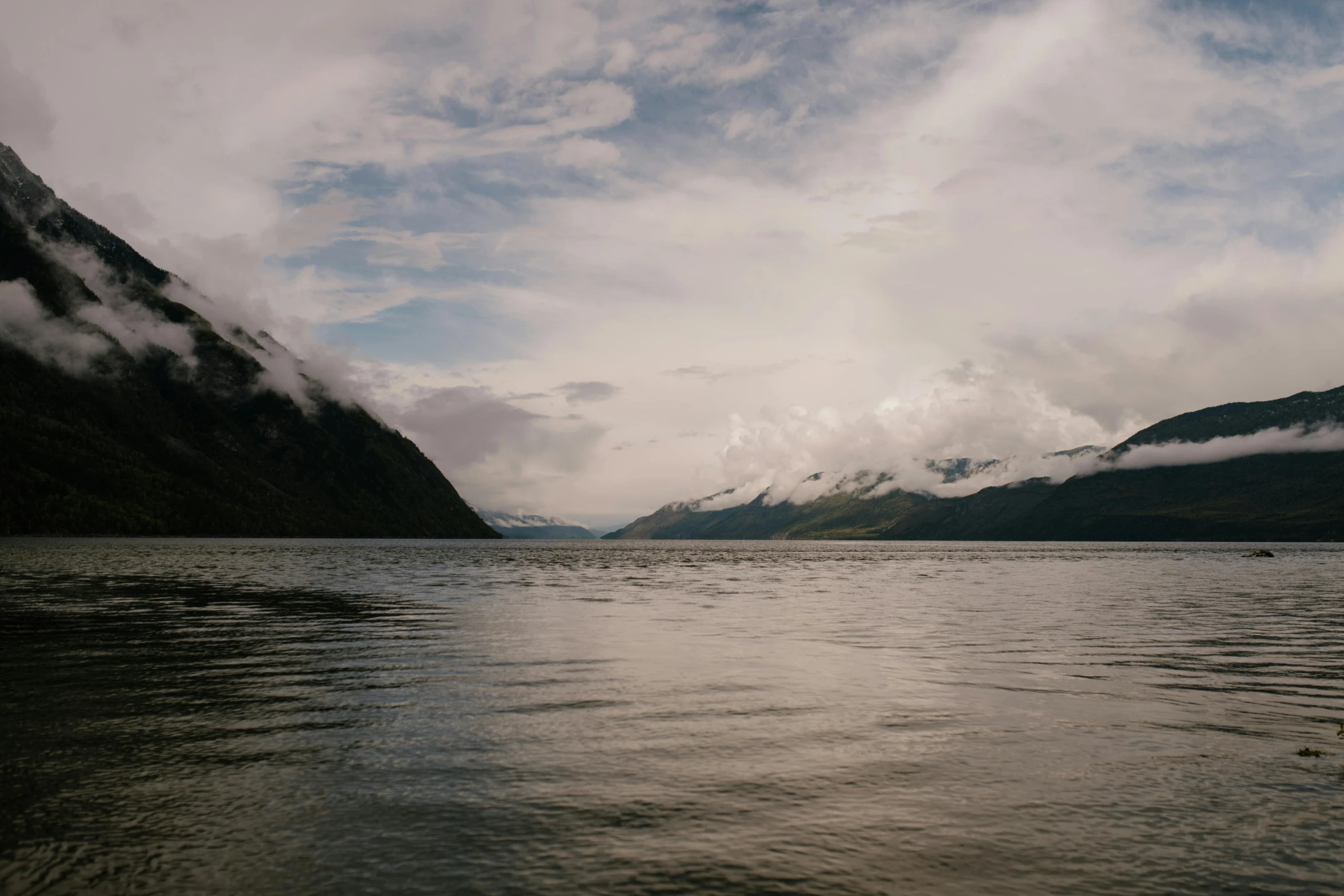 a body of water with mountains in the background, by Kristin Nelson, trending on unsplash, grey clouds, fjord, low quality photo, ash thorp khyzyl saleem