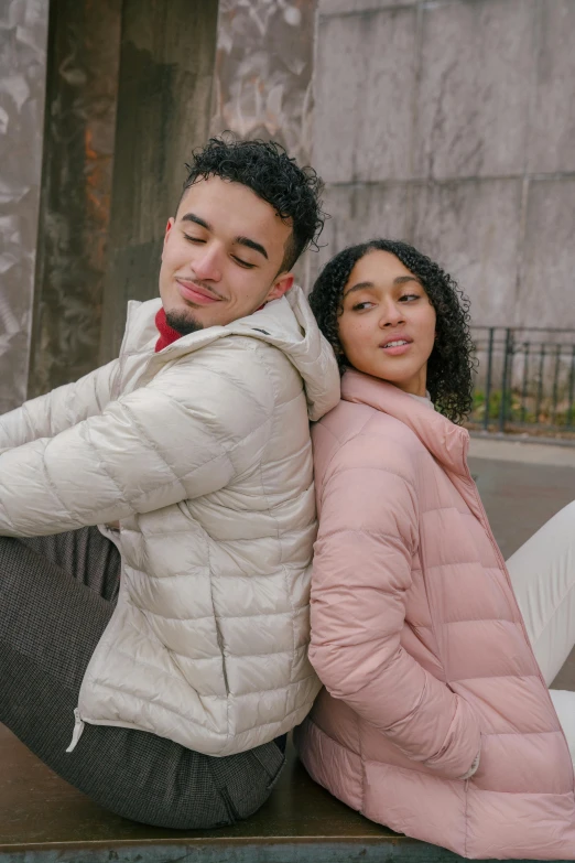 a man and a woman sitting next to each other, model wears a puffer jacket, muted pastels, highly upvoted, hispanic