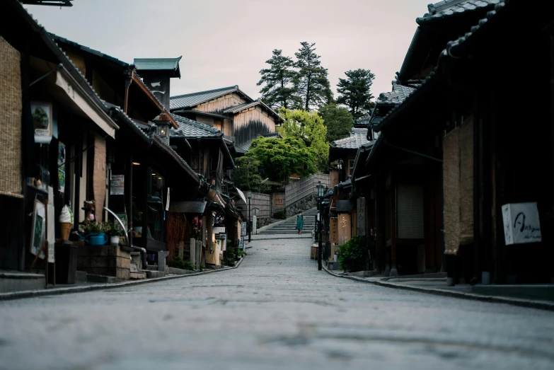 a person is walking down a narrow street, inspired by Kaii Higashiyama, unsplash contest winner, mingei, old village in the distance, peaked wooden roofs, slightly pixelated, early evening