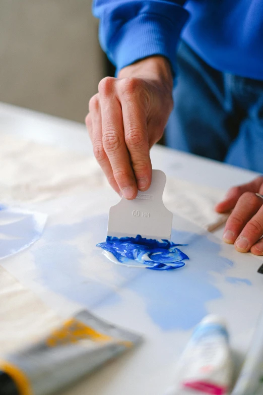 a close up of a person painting on a table, a silk screen, inspired by Yves Klein, unsplash, soap carving, spatula, seaside, wearable art