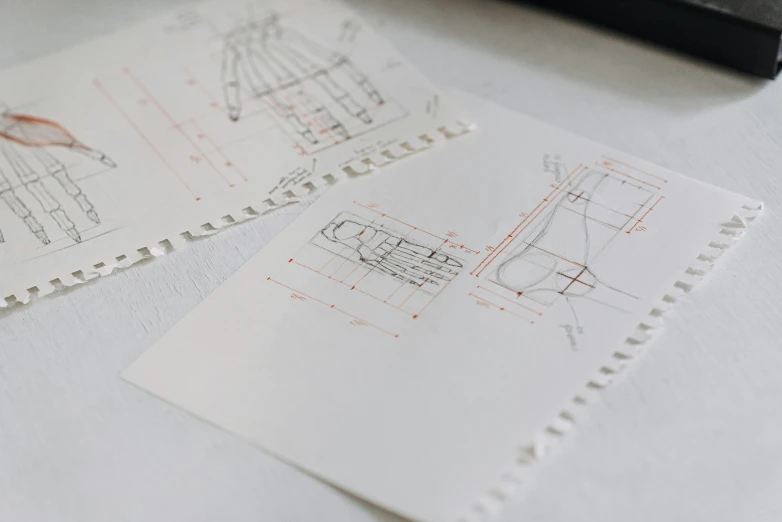 a piece of paper sitting on top of a table next to a pair of scissors, a drawing, by Emma Andijewska, technical drawings, drawn on white parchment paper, beautiful plans, robot design