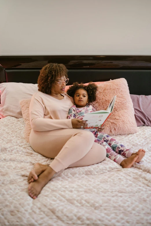 a woman reading a book to a child on a bed, sleepwear, brown and pink color scheme, african american woman, manuka