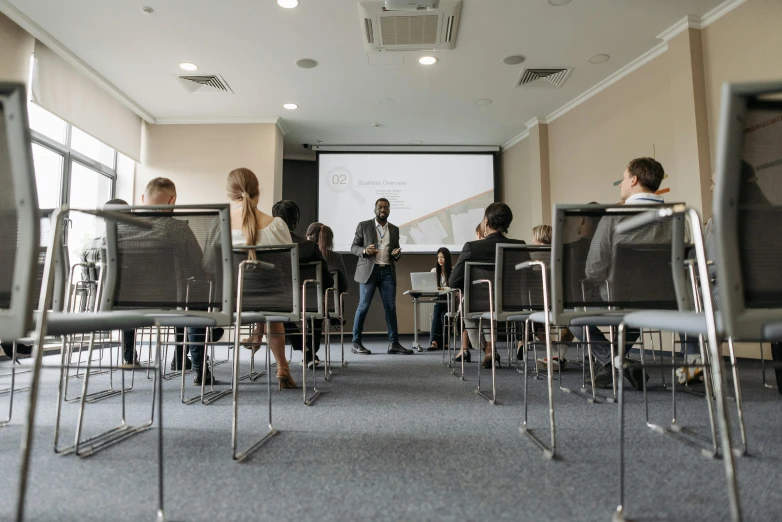 a group of people sitting in chairs in a room, teaching, 15081959 21121991 01012000 4k, lachlan bailey, a person standing in front of a