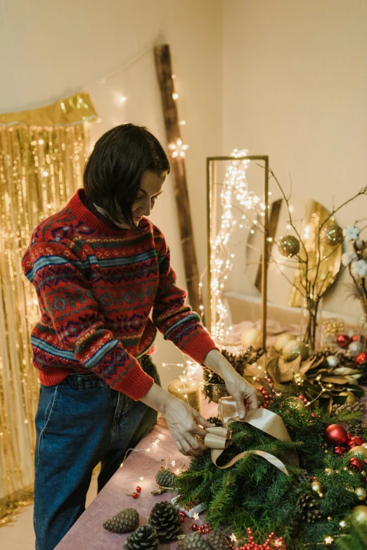 a woman cutting a wreath on top of a table, by Julia Pishtar, pexels, lots of lights, wearing casual sweater, handsome man, sequins