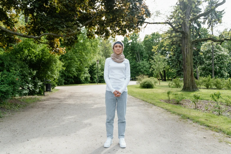 a woman standing in the middle of a road, inspired by Valéria Dénes, hurufiyya, standing in a botanical garden, wearing a tracksuit, in white clothes, at a park