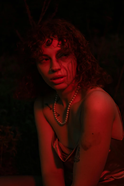 a woman sitting on top of a bed under a red light, an album cover, inspired by Nan Goldin, pexels contest winner, renaissance, frank dillane as a satyr, in the woods at night, red birthmark, curly bangs