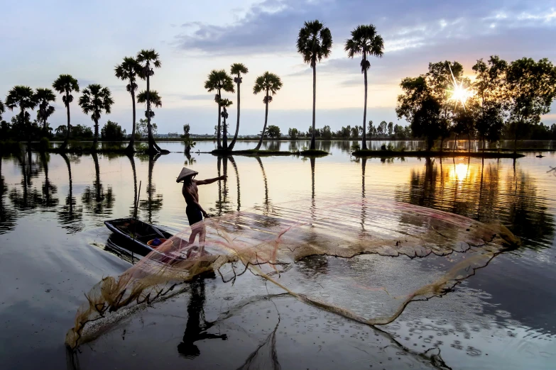 a man that is standing in the water with a net, inspired by Steve McCurry, pexels contest winner, futuristic phnom-penh cambodia, coconut trees, evening sun, fishing