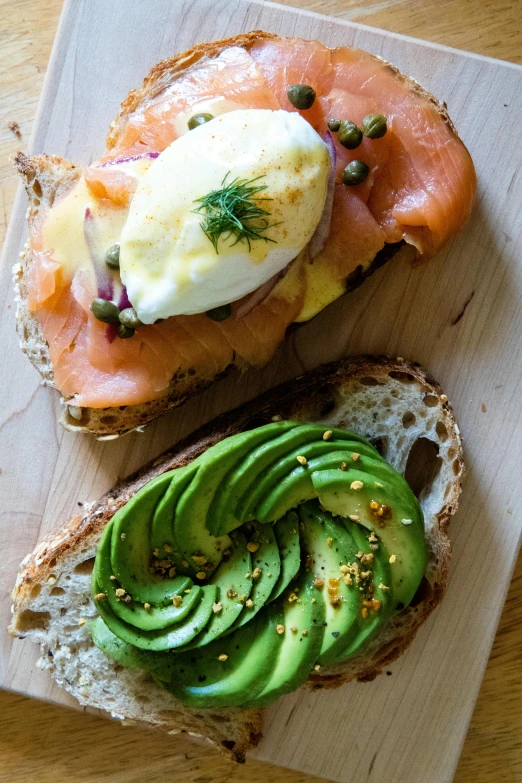 a wooden cutting board topped with a sandwich and avocado, by Leo Michelson, salmon, eggs, nordic